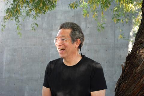 Sesshu Foster laughs while wearing clear-rimmed glasses and a black t-shirt