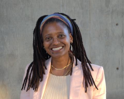 Tracy K. Smith wears a pink blazer and cream dress while standing in front of a grey concrete wall