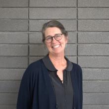 Sally Ball wears glasses, silver hoop earrings, gray shirt and navy blue cardigan.